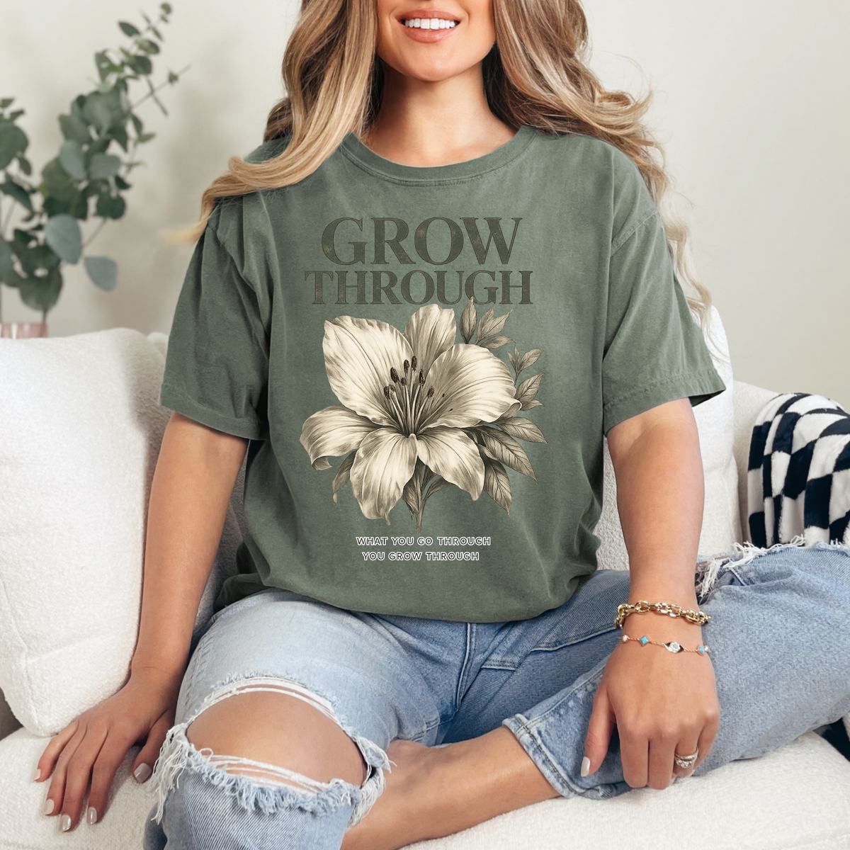 Woman wearing a green t-shirt with a floral design and text, sitting on a couch.