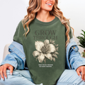 Person wearing a green sweatshirt with a floral design and text, sitting on a light-colored couch.