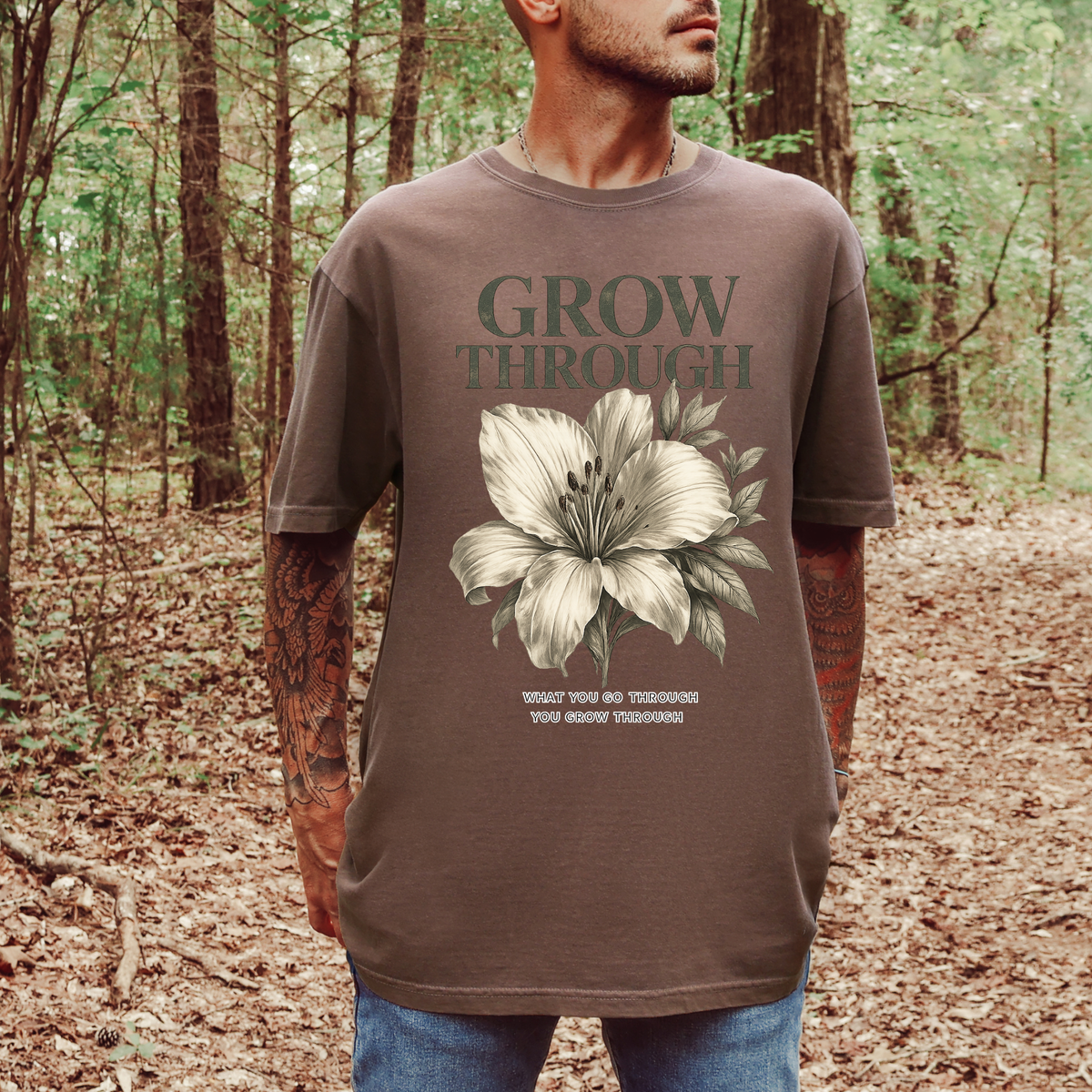 Person wearing a brown t-shirt with a floral design and text in a forest setting