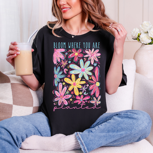 Person wearing a black t-shirt with colorful floral design and text, sitting on a couch.