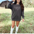 Woman wearing a dark gray sweatshirt with text in a field with a wooden structure in the background