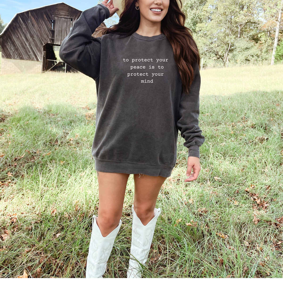 Woman wearing a dark gray sweatshirt with text in a field with a wooden structure in the background