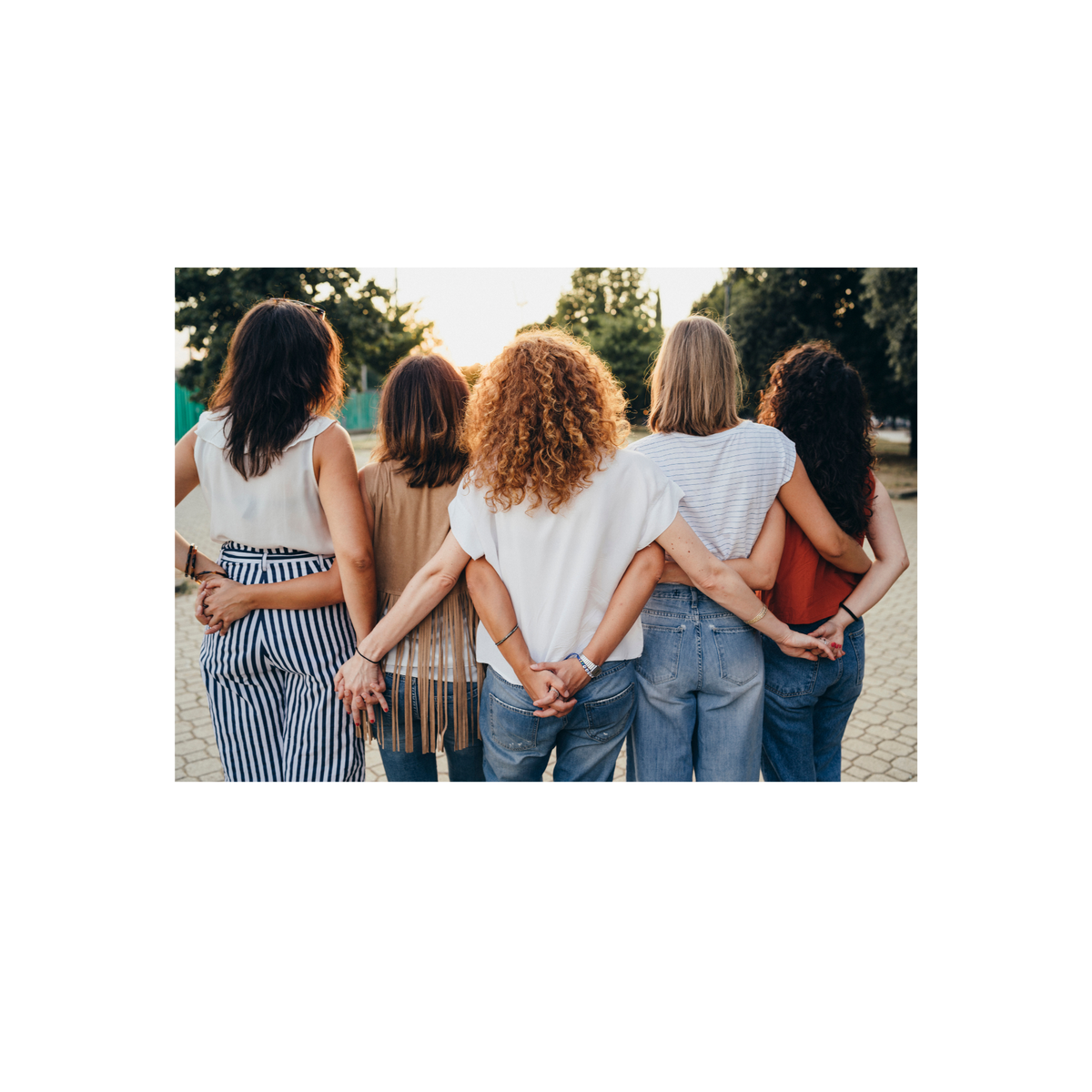 A group of five women standing outdoors with their backs to the camera, holding hands and wearing casual clothing in a sunny park setting.