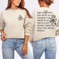 Person wearing a beige sweatshirt with a floral design on the front and text on the back, standing against a light gray background.